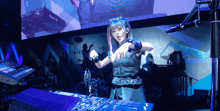 a girl with blue hair is standing in front of a dj mixer and giving a thumbs up