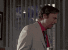 a man in a white suit and red tie stands in front of a window