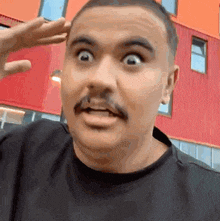 a man with a mustache is wearing a black shirt and making a funny face .