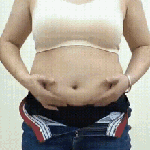 a woman is holding her stomach with both hands while wearing a bra and jeans .