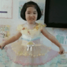 a little girl in a yellow and pink dress is standing in front of a tv .