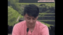 a young man in a pink shirt is talking into a microphone .