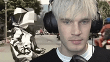 a man with white hair is wearing headphones and holding a microphone while standing on a street .