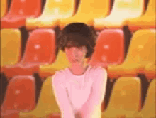 a girl in a pink shirt is standing in front of a row of yellow and red chairs .