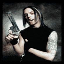 a man with long hair and a tattoo on his arm holds a gun