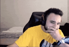 a man wearing headphones and a yellow shirt covering his mouth with his hand