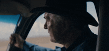 a man in a cowboy hat is driving a car in the desert