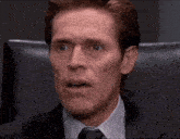 a man in a suit and tie is sitting in a chair making a funny face .
