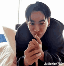 a man is laying on a bed with his hands folded in front of his face and making a heart shape with his fingers .