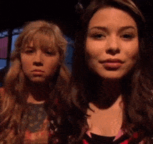 two girls are standing next to each other in a dark room and looking at the camera .