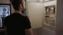 a man in a black shirt is looking into a medicine cabinet with a box of tylenol in it