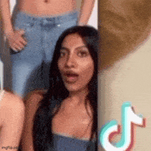 a woman with long black hair is standing next to a wall with a tiktok logo .
