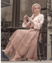 a woman in a hijab sits in a chair holding a cup