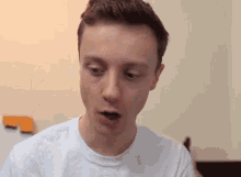 a young man wearing a white t-shirt is looking at the camera