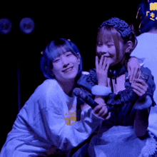 a girl with blue hair is hugging another girl who is wearing an apron