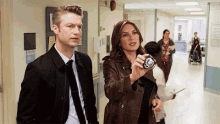 a man in a suit and tie stands next to a woman in a brown jacket