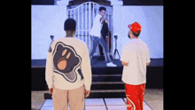 two men standing on a stage with one wearing a sweater with a bear on the back