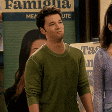 a man in a green sweater stands in front of a poster that says famiglia