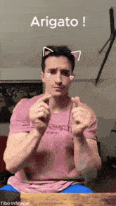 a man in a pink shirt with cat ears making a heart sign