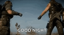 two men in military uniforms are standing next to each other in the desert and giving each other a fist bump .