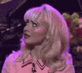 a woman with blonde hair and pink makeup is standing in front of a piano and flowers .
