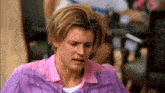 a man with blonde hair is wearing a pink shirt and a purple shirt .