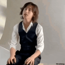 a young man wearing a vest and a white shirt is sitting on a stool .
