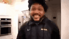 a man wearing a michigan sweatshirt smiles while standing in a kitchen