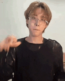 a young man wearing glasses and a black shirt is making a gesture with his hand .