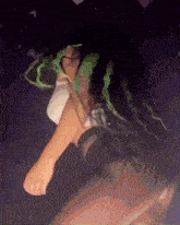 a woman with long green hair is dancing in a dark room .