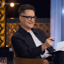 a man wearing glasses is sitting in a chair with a pen in his hand