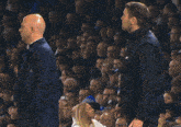 a man in a trench coat stands next to another man in a blue and white striped shirt