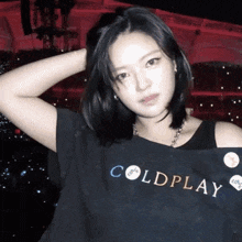 a woman wearing a black coldplay t-shirt is standing in front of a stage .