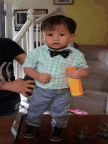 a little boy wearing a bow tie holds a bottle