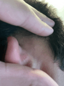 a close up of a person 's ear with a hand on it