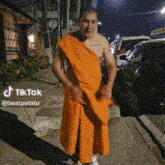 a man in an orange robe is standing on a sidewalk .
