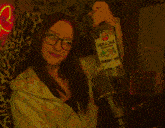 a woman with glasses is holding a bottle of ioram vodka over her head