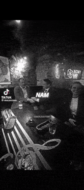 a black and white photo of people sitting at a table with the word nam on the table