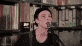 a young man in a black hat is singing into a microphone in front of a bookshelf .