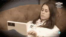 a woman is laying on a couch using a laptop .