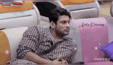 a man is sitting on a couch with a pillow that says sid 's princess .