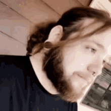 a man with a beard and long hair is wearing a black shirt and earrings .