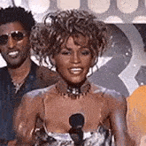 a woman is standing in front of a microphone and smiling while standing next to two men .
