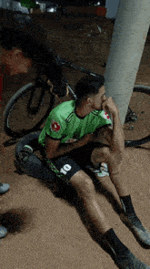 a man wearing a green shirt with the number 10 on it sits on the ground