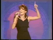 a woman in a black dress is singing into a microphone on a stage