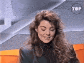 a woman with long curly hair is smiling in front of a sign that says top on it