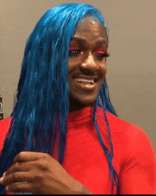 a woman with blue hair is smiling and wearing a red top