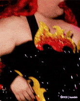 a woman with red hair is wearing a black top with a yellow and red design