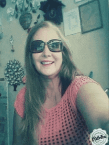 a woman wearing sunglasses and a pink shirt is smiling