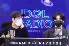 two men wearing face masks are sitting in front of a mbc radio x universe sign .
